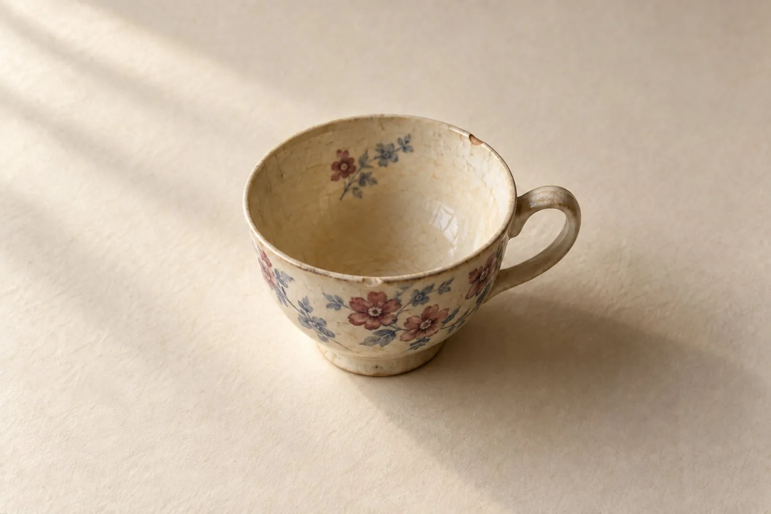 Une tasse en céramique crème à fleurs bleues et bordeaux avec un petit éclat sur le bord
